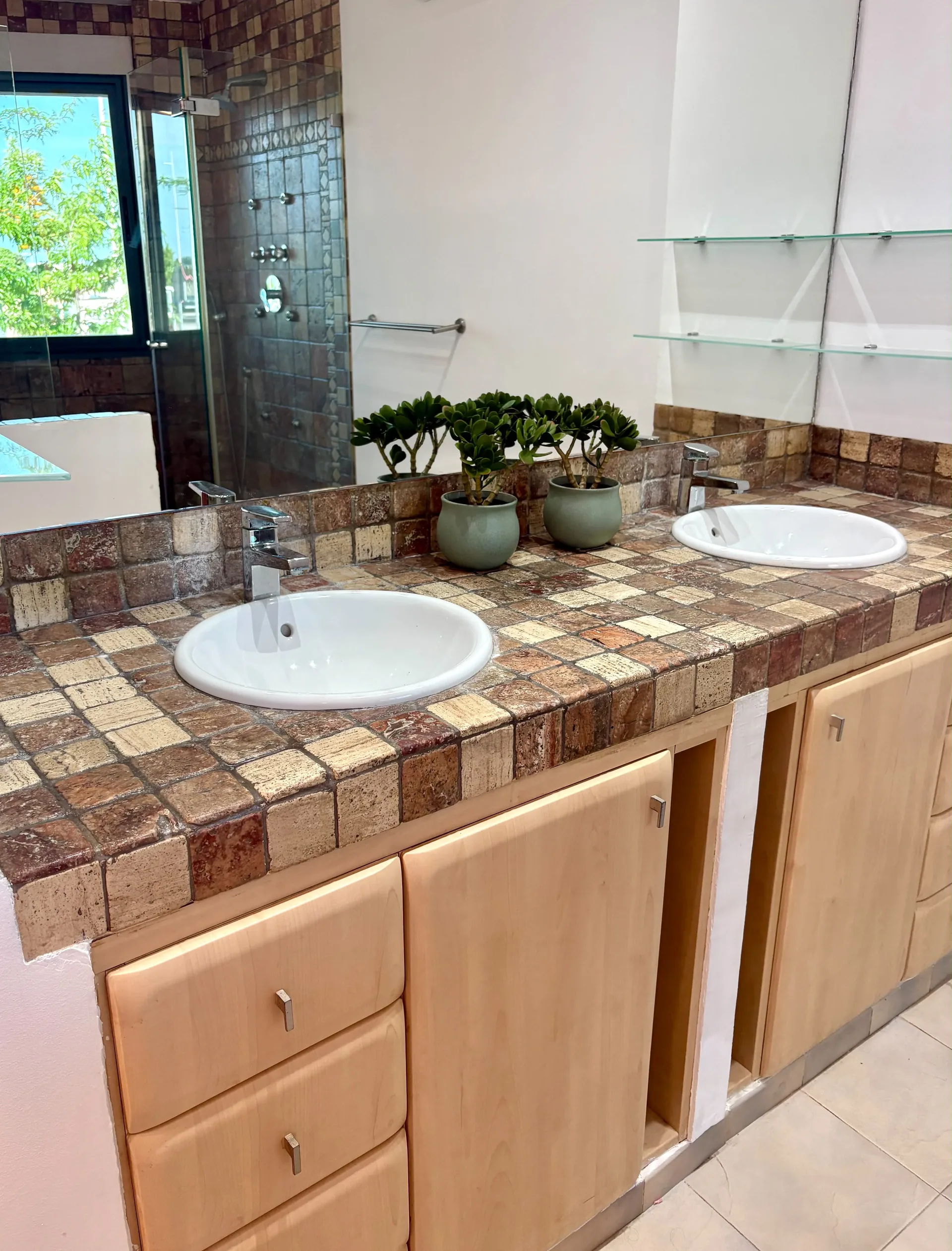 Baño principal con doble lavabo redondo empotrado en encimera de mosaico marrón y plantas decorativas — Chalet Treviso Gandía